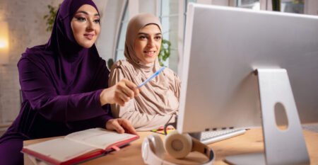 Happy two muslim women at home during lesson, studying near computer, online education